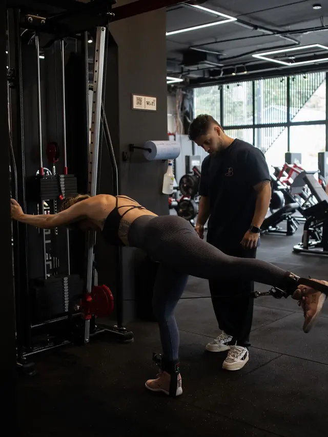Personal trainer acompanhando a execução de uma aluna no exercício de glúteo no cabo